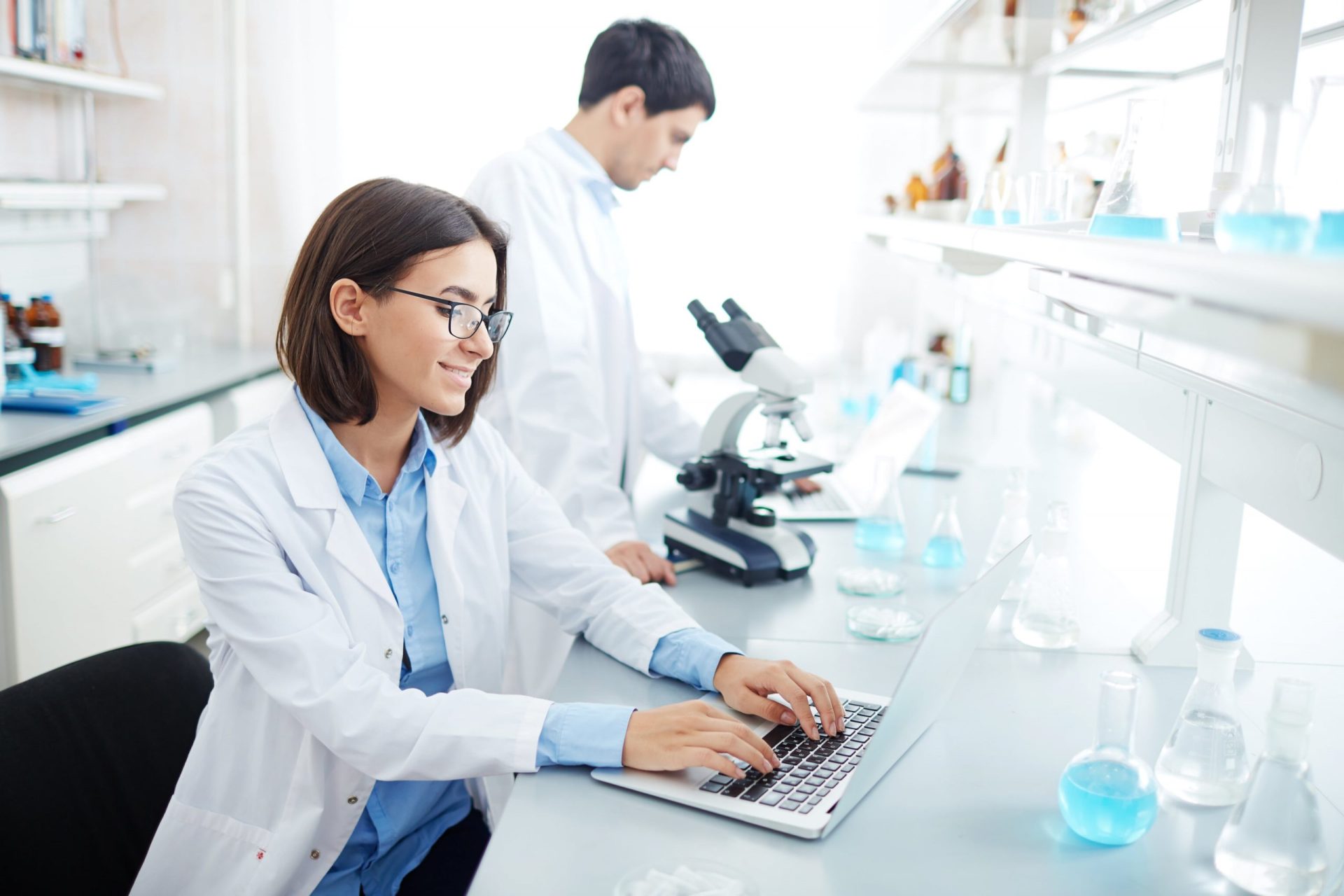 Scientist typing data on a laptop in a modern laboratory, showcasing advanced research and technology equipment.