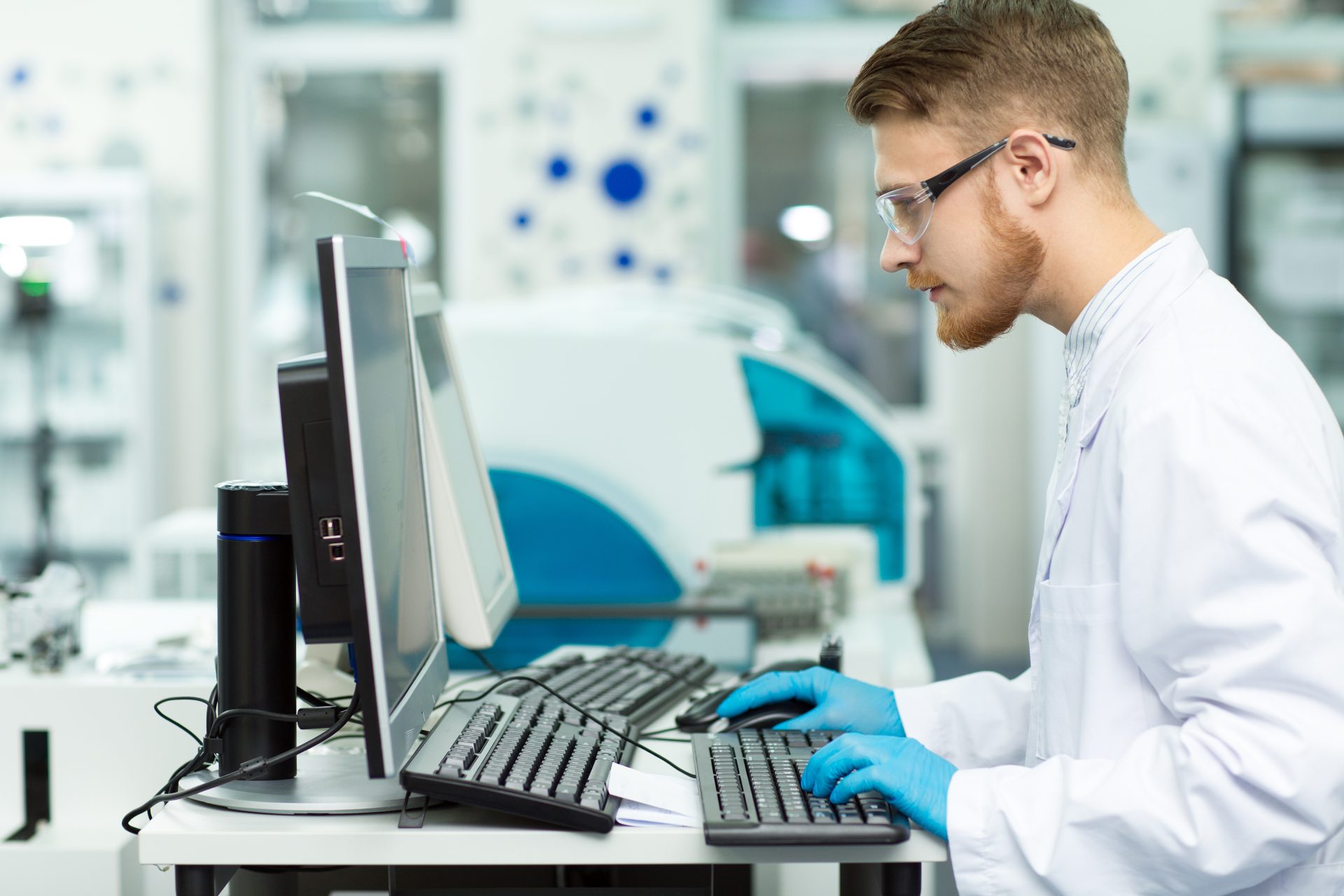 A scientist wearing protective eyewear and gloves works at a computer station in a laboratory. The image suggests the use of a Laboratory Information Management System (LIMS) and an Electronic Laboratory Notebook (ELN) to manage and document experimental data.