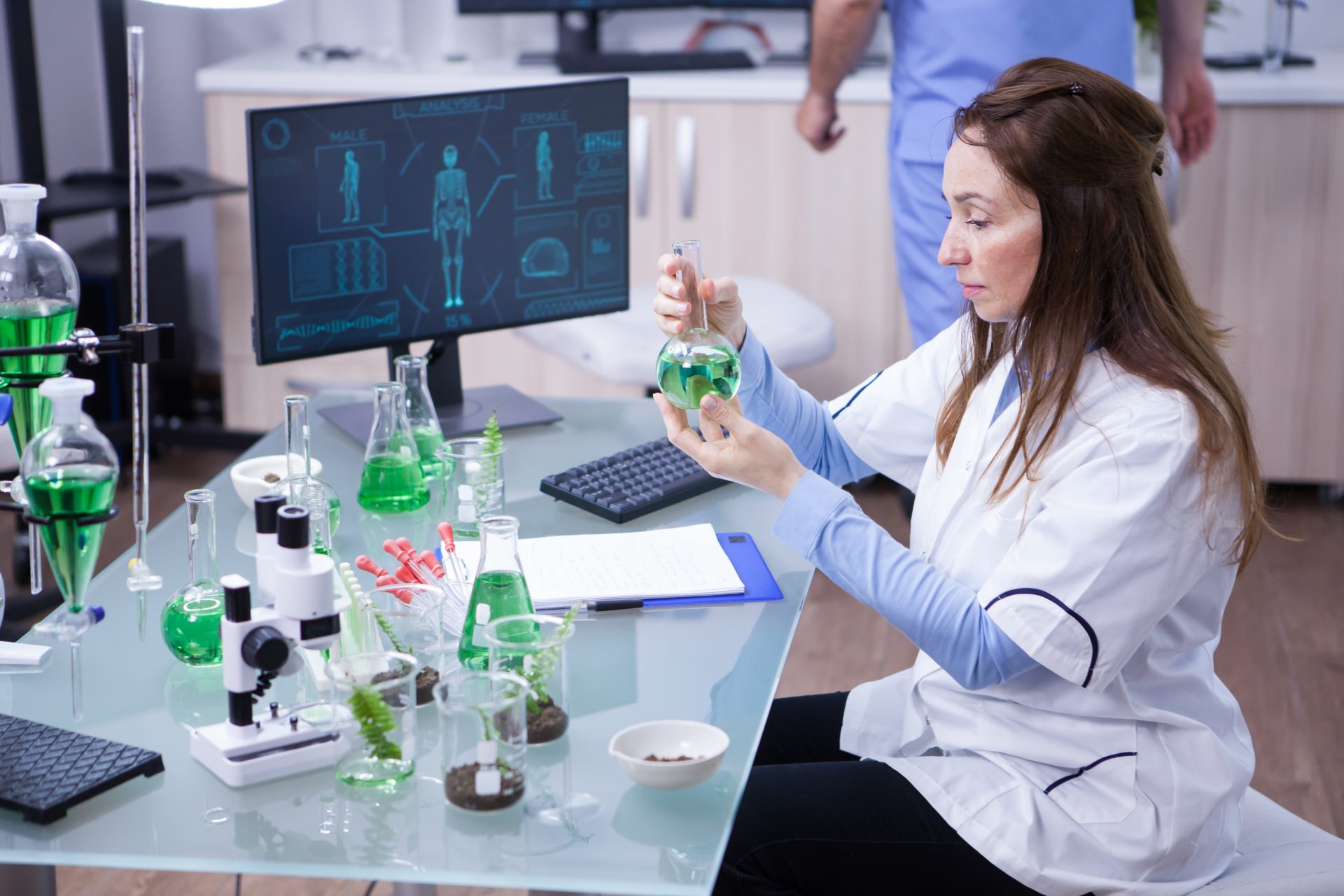 . A woman in a lab coat carefully examines a green liquid in a laboratory setting, showcasing her scientific expertise.