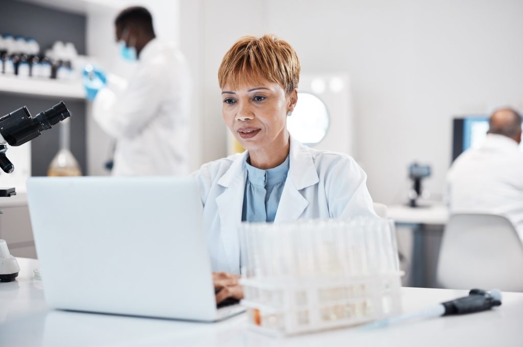 A woman in a lab coat operating a laptop, representing the intersection of technology and scientific inquiry.