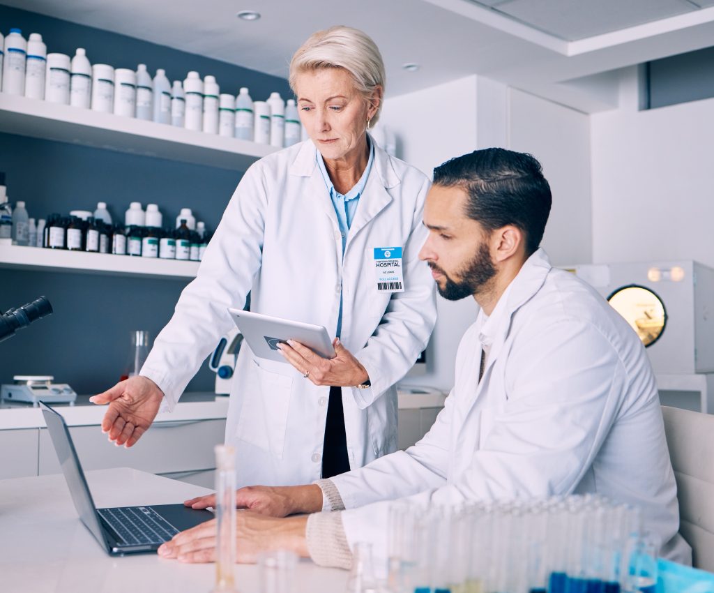 Two scientists in lab coats reviewing information on a laptop, demonstrating teamwork and collaboration in a research laboratory.