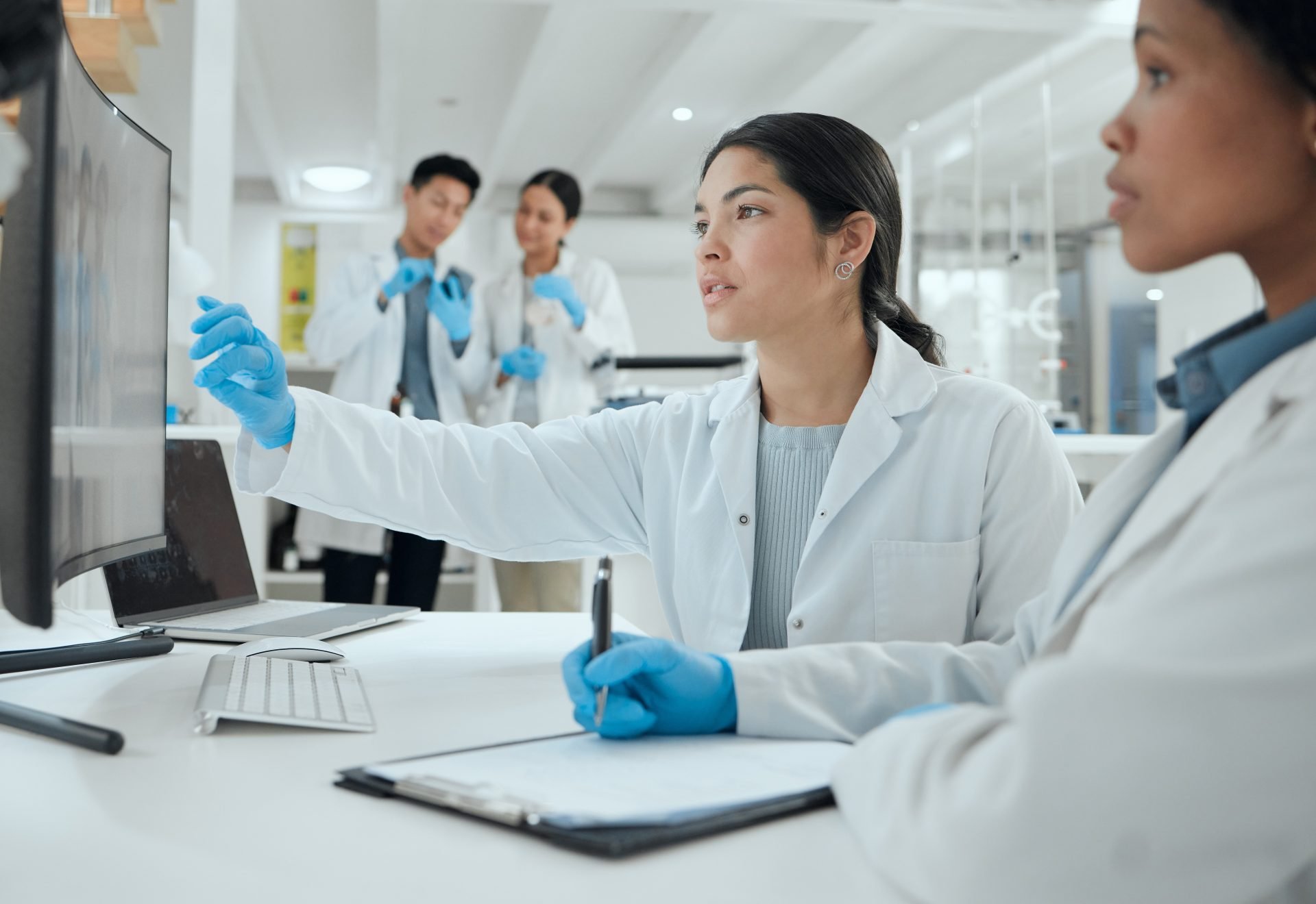 A team in lab coats and gloves observes a computer screen, engaged in research or analysis within a laboratory.